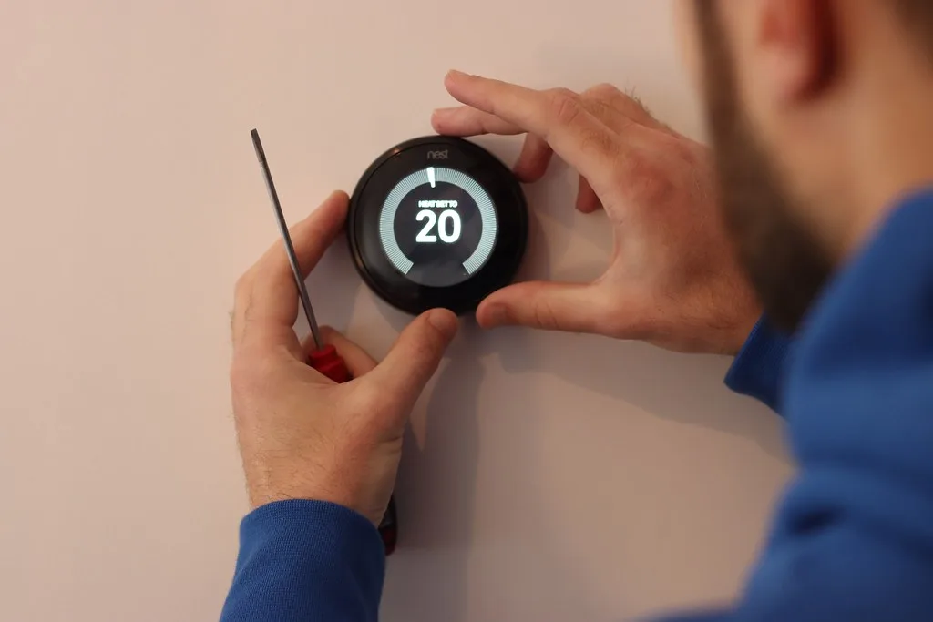 Technician mounting a smart thermostat base on an interior wall
