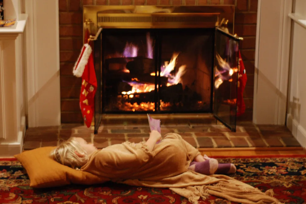 An armchair and a pot of tea beside a crackling fire