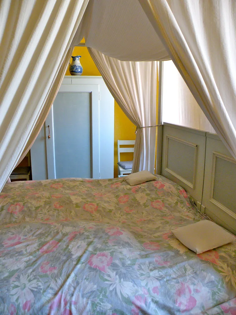 Guest room with a white-curtained four-poster bed and antique chairs